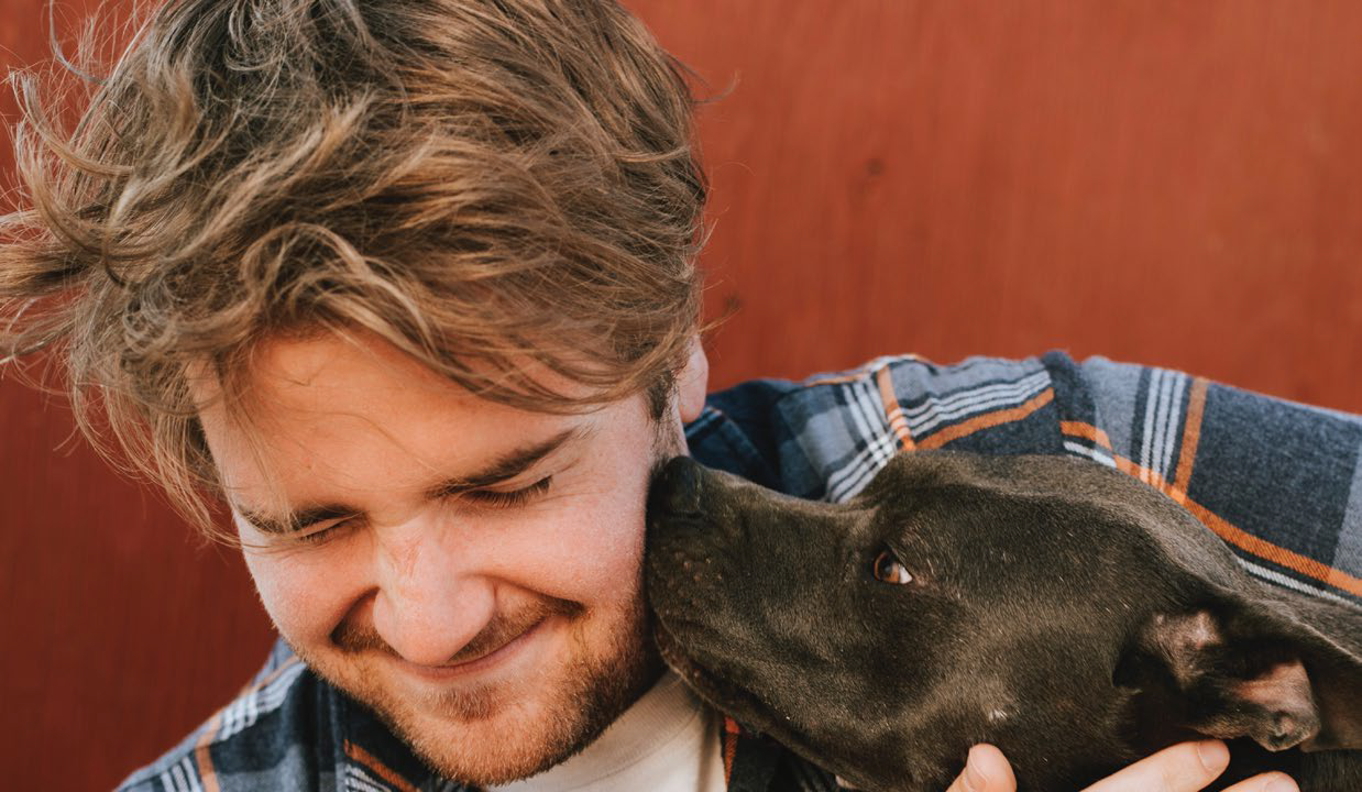 Man smiles slightly while getting licked on the face by dog