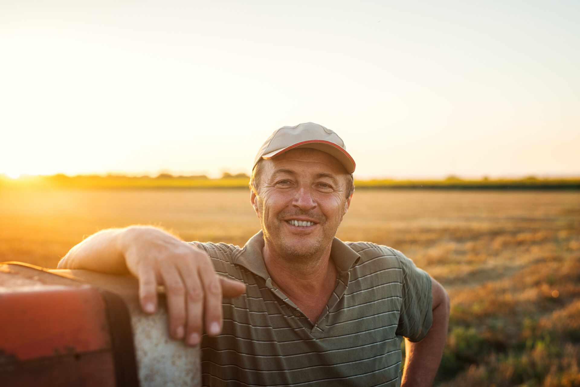 A farmer leans against his tractor at sunset