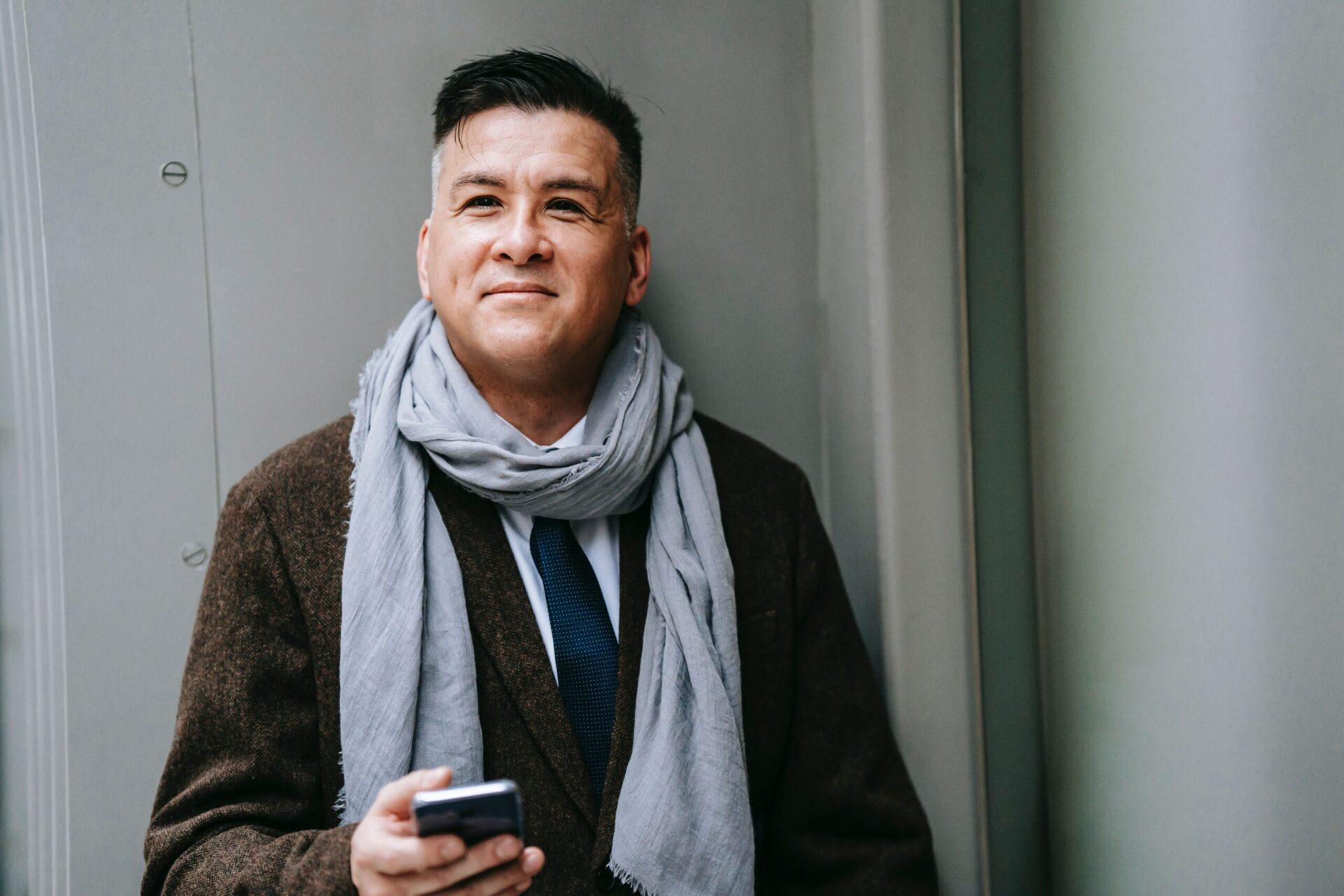 A man with a suit and a scarf smiles up from his phone A man with a suit and a scarf smiles up from his phone
