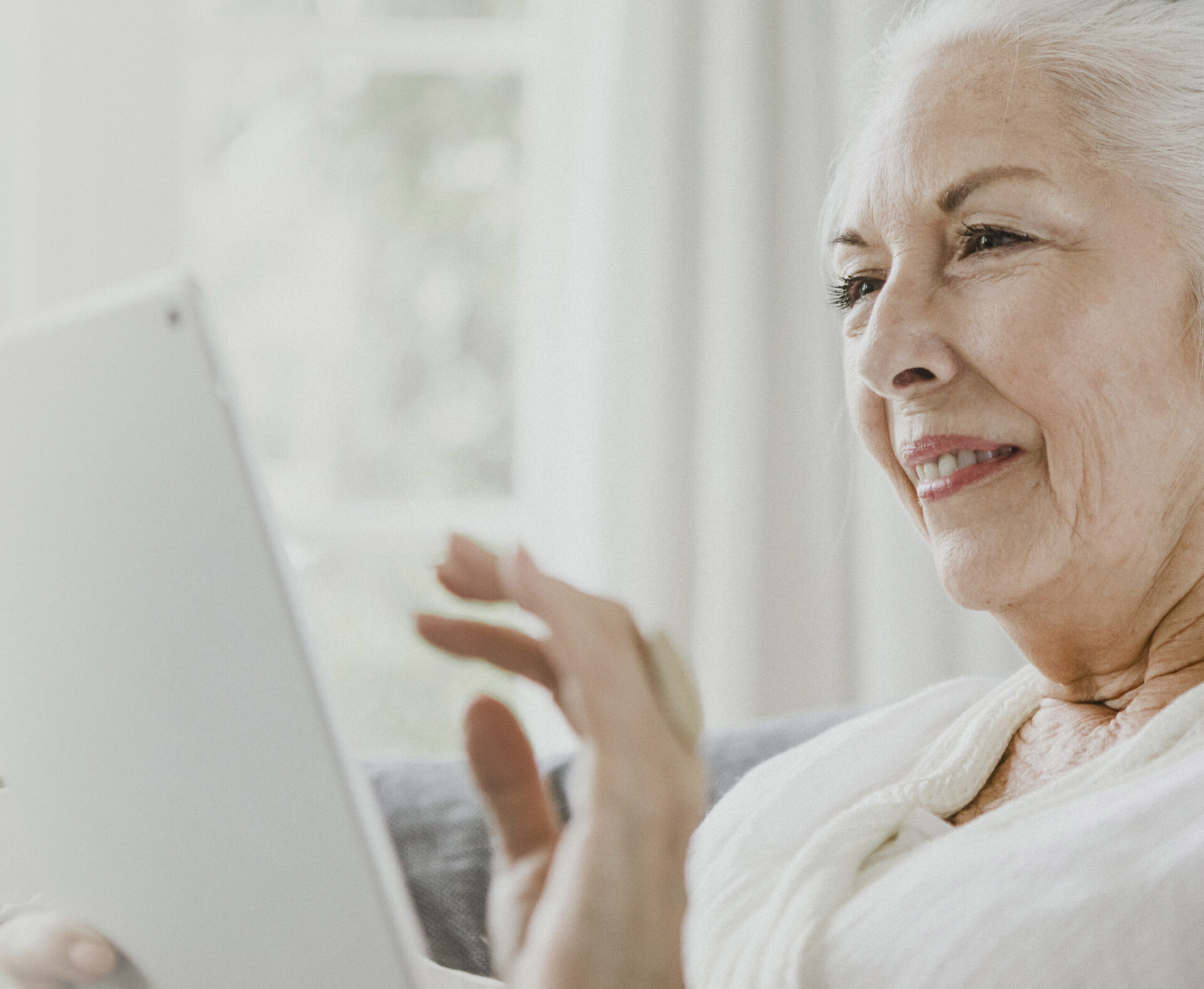 An older lady uses a laptop while smiling