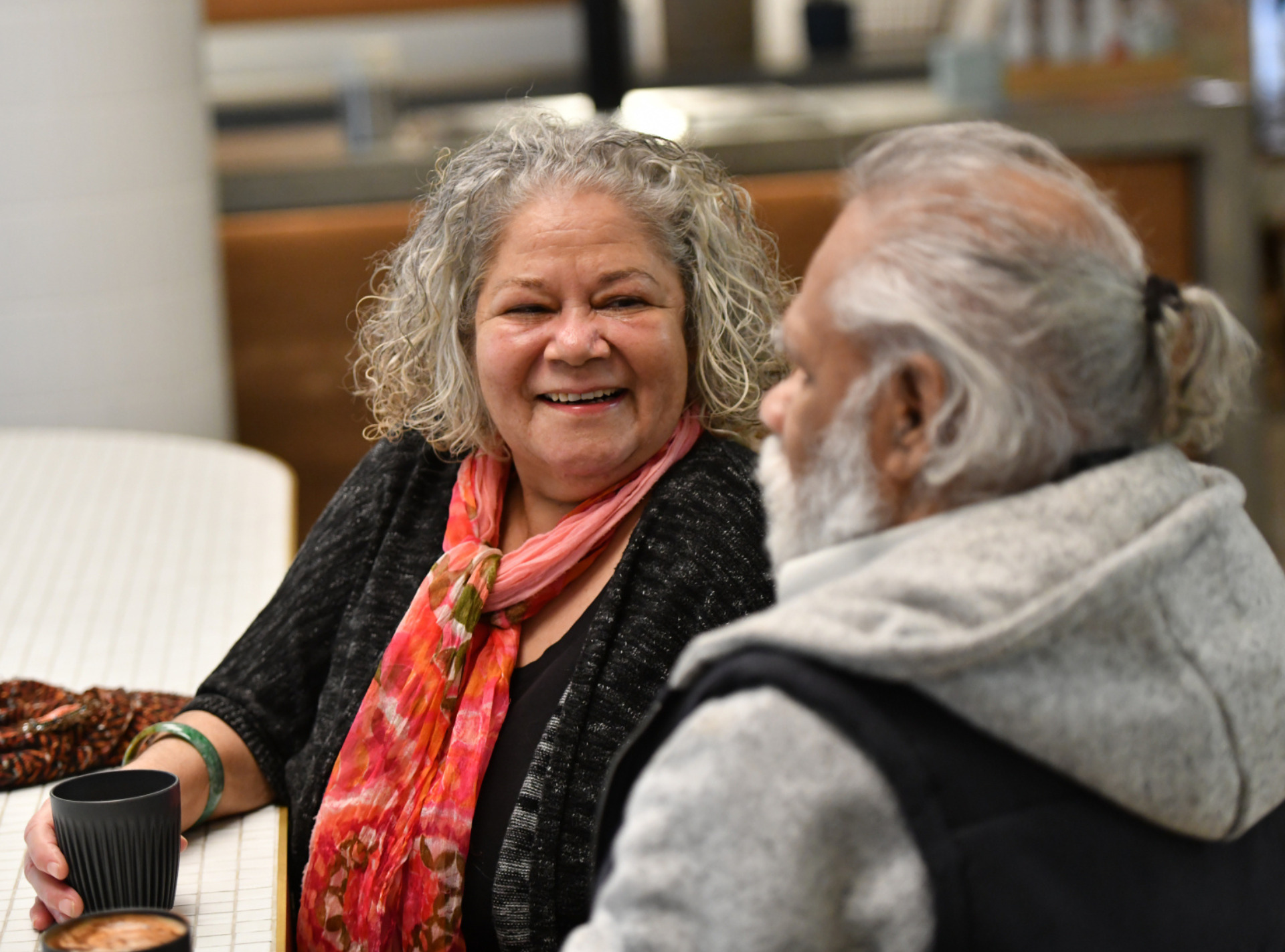 An Indigenous man and woman sit together enjoying a coffee.